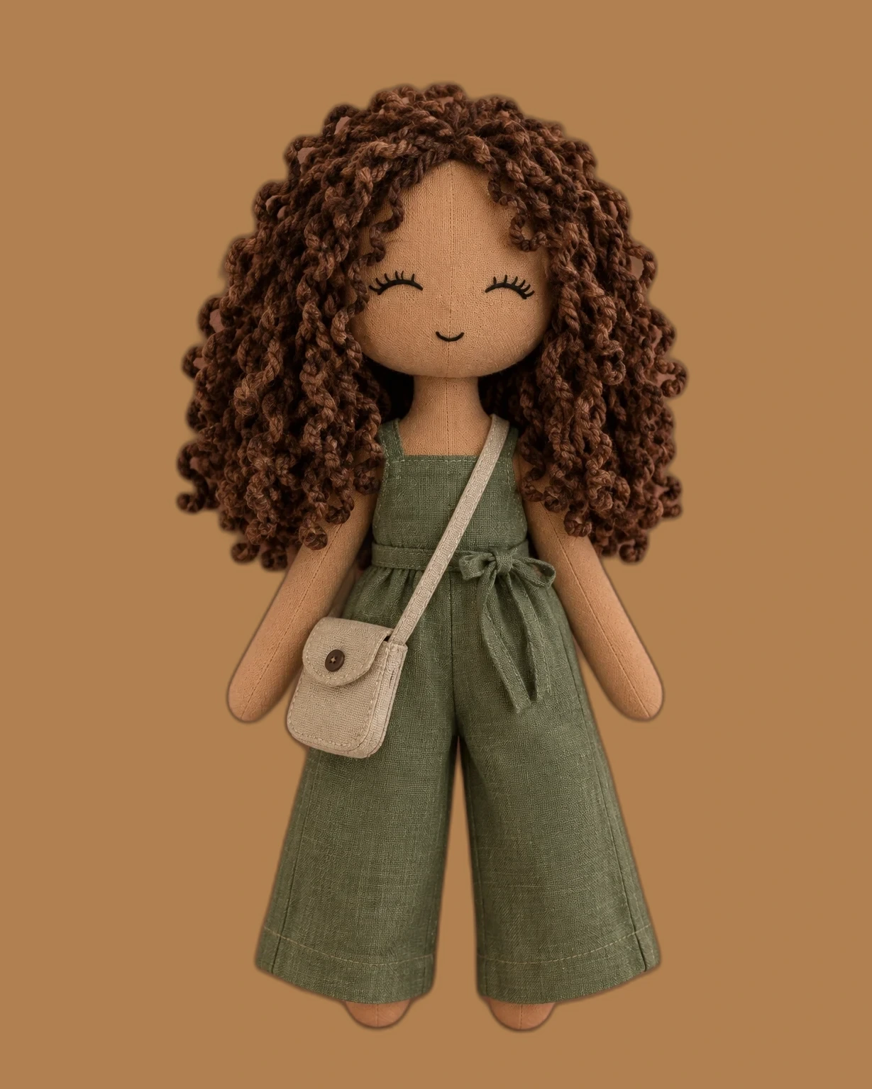Doll with brown curly hair in a sage-green linen jumpsuit, carrying a cream crossbody bag
